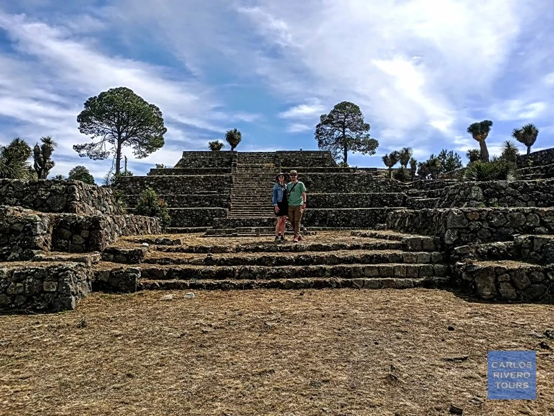 Couple posing for a photo in a ceremonial plaza at Cantona, surrounded by ancient stone architecture and pre-Hispanic landscapes.
