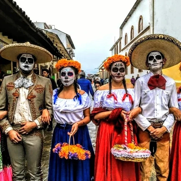 Youth in Mexican regional attire with skull-painted faces during Day of the Dead festivities.