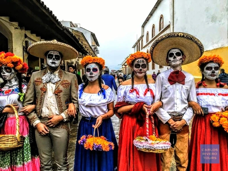 Youth in Mexican regional attire with skull-painted faces during Day of the Dead festivities.