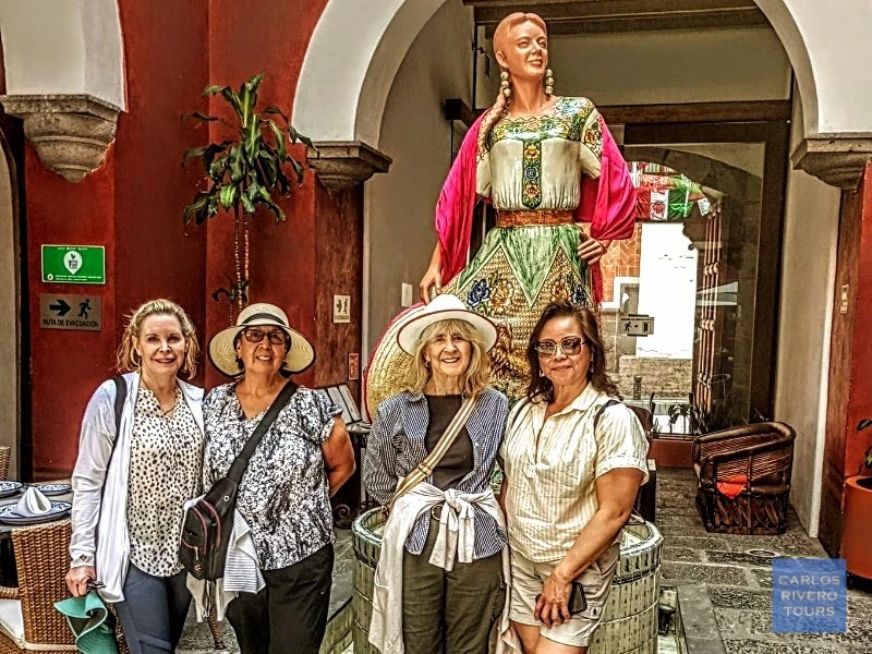Women enjoying the Puebla City Tour, posing by the Talavera sculpture honoring a famous woman from Puebla, celebrating local artistry, feminine legacy, and urban heritage.