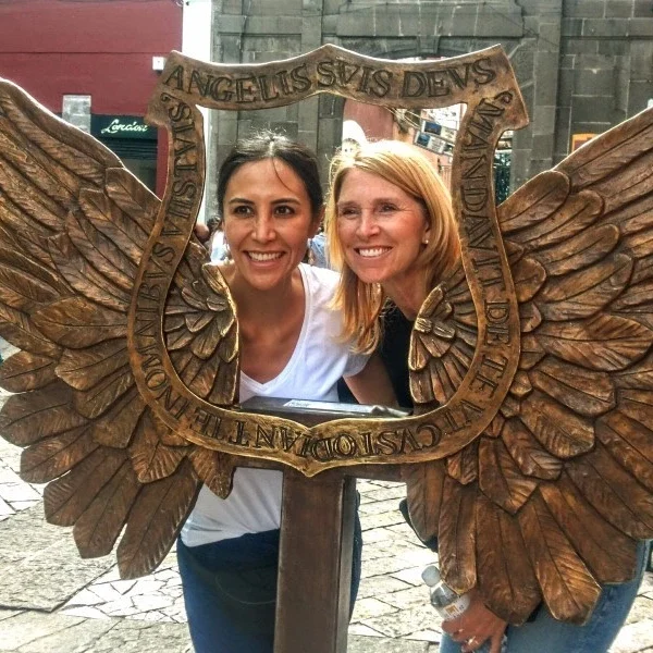Two female visitors posing with street art referencing Puebla’s original name, Puebla de los Ángeles, a UNESCO World Heritage city known for its colonial legacy.