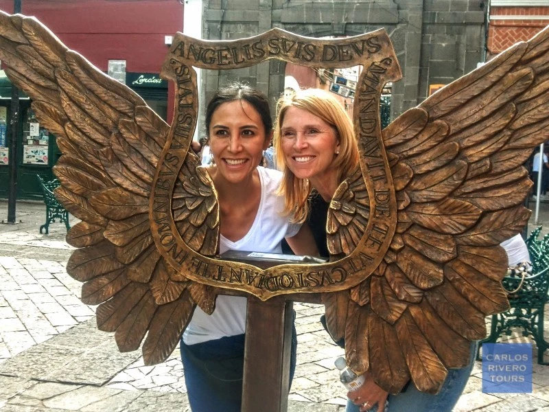 Two female visitors posing with street art referencing Puebla’s original name, Puebla de los Ángeles, a UNESCO World Heritage city known for its colonial legacy.