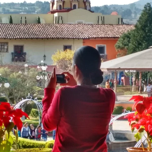 Woman taking photos of the Zócalo in Zacatlán, capturing the charm of this Magic Town with its colonial buildings, floral clock, and festive atmosphere.