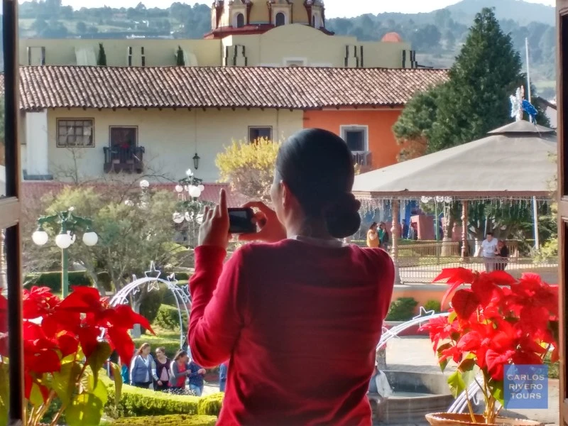Woman taking photos of the Zócalo in Zacatlán, capturing the charm of this Magic Town with its colonial buildings, floral clock, and festive atmosphere.
