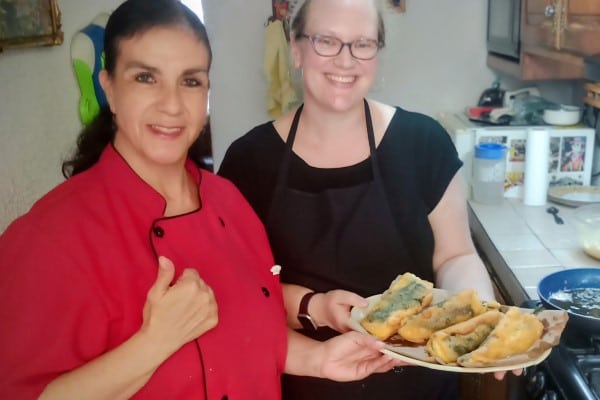 Traditional Puebla-style chiles rellenos being delicately battered and pan-fried to a golden finish during a hands-on Mexican cooking class.